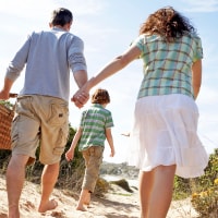 Parents holding hands while walking to the beach with their 10 year old son.