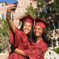 Happy college graduates taking photo with smartphone