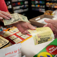A person exchanges a $20 bill for mega millions tickets over the counter at a Save 'N Time store