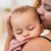 Mother Cuddling Sleeping Baby Daughter At Home