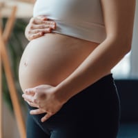 Side view close-up of pregnant woman touching her belly. 