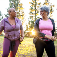 Two black woman walking through a grass field.