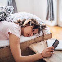 Sleepy young woman waking up and looking at her phone.