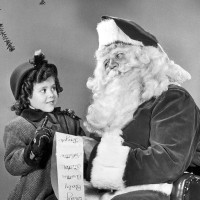 A little girl giving Santa Claus her wish list surrounding by packages and toys, 1945.