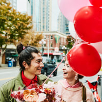 Smiling couple walking down city sidewalk with flowers and balloons during Valentines date