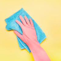 Hand in pink glove with cleaning rag on yellow background