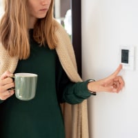 Woman with tea cup adjusting thermostat