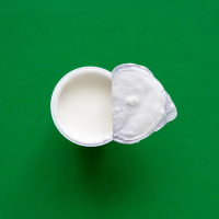 An opened plastic yogurt cup on a green background