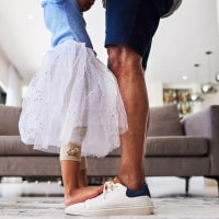 Feet, dance and girl dancing with father in a living room, love and family fun in their home together. Shoes, happy family and parent teaching child dancer, loving and caring support by single dad