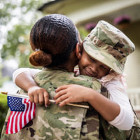Daughter embracing female U.S. soldier mother in front of home
