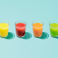 Four glasses of different colored juice on a colorful background.