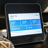 A Square payment device displays tipping options at a coffee shop next to a basket of dollar tips