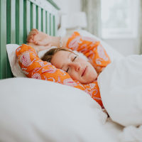 A young woman in orange pyjamas is fast asleep in a double bed