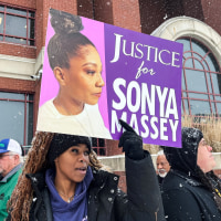 A woman holds a sign that reads "Justice for Sonya Massey"