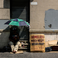 A homeless person holds an umbrella to block out the sun