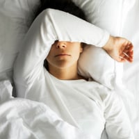 Woman lying down in bed and crying covering her face.