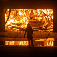 A firefighter observes a burning garage and car.