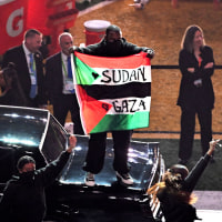 A protestor holds a Palestinian flag with the words "Gaza" and "Sudan" as US rapper Kendrick Lamar performs during Apple Music Halftime Show.