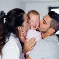 Portrait of young couple with toddler girl in the morning indoors in bathroom at home, kissing.