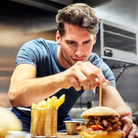Chef preparing burger on wooden plate.