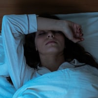 Woman in bed covering eyes with hands.