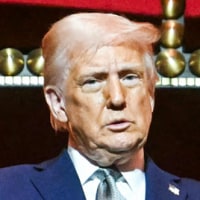 Donald Trump, with both hands raised, stands on a balcony inside of a building