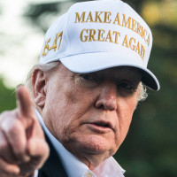 Donald Trump points and wears a white hat that says "Make America Great Again"