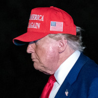Donald Trump walks outside wearing a red MAGA hat, side profile