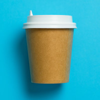 Disposable paper cup with lid for coffee on a bright pastel blue background.