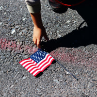 A boy reaches over to pick up a U.S. flag