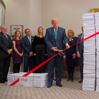 President Donald Trump uses gold scissors to cut red tape between  stacks of papers representing government regulations on Dec. 14, 2017, at the White House.