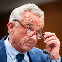 Robert F. Kennedy holds the side of his glasses that he's wearing