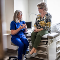 Female doctor in scrubs consulting with senior woman in exam room