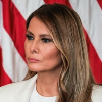 Melania Trump seated in front of an American flag backdrop