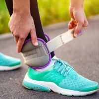 Athletic woman puts on ankle weights for walking outdoors.
