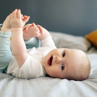 A 6 month old baby boy smiling, laying on a bed.