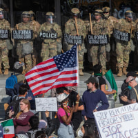 Demonstrators holding signs and flags face California National Guard members standing guard outside the Federal Building 