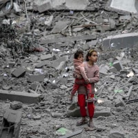 A Palestinian girl carries a child through the rubble of houses destroyed by Israeli bombardment in Gaza City 