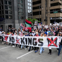 A large group of people walk through a street and hold a banner that says "No Kings"