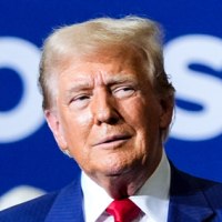 Donald Trump stands on stage in front of workers wearing safety vests