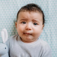 Baby girl lying in crib with funny worried face and holding a stuffed rabbit.
