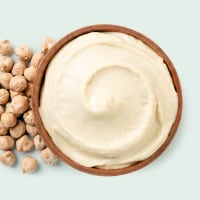 Bowl of hummus with chickpeas on a color background.
