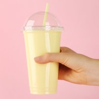 Woman holding plastic cup of tasty smoothie on pink background, closeup
