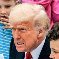 President Donald Trump shows a group of children a trading card of himself while sitting outside
