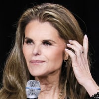 Maria Shriver holds a microphone while seated on stage