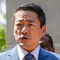Gene Wu speaks at a podium outside surrounded by other people