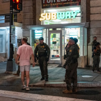 A man walks near officers outside of a Subway location holding a sandwich