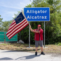 A man wearing a "Make America Great Again" hat waves a flag outside the detention center called "Alligator Alcatraz" near Ochopee, Fla., on July 12 , 2025. 