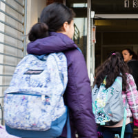 Two people greet students as they enter a school building