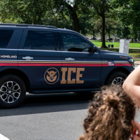 An Immigration and Customs Enforcement police SUV patrols on the road as people watch from the sidewalk